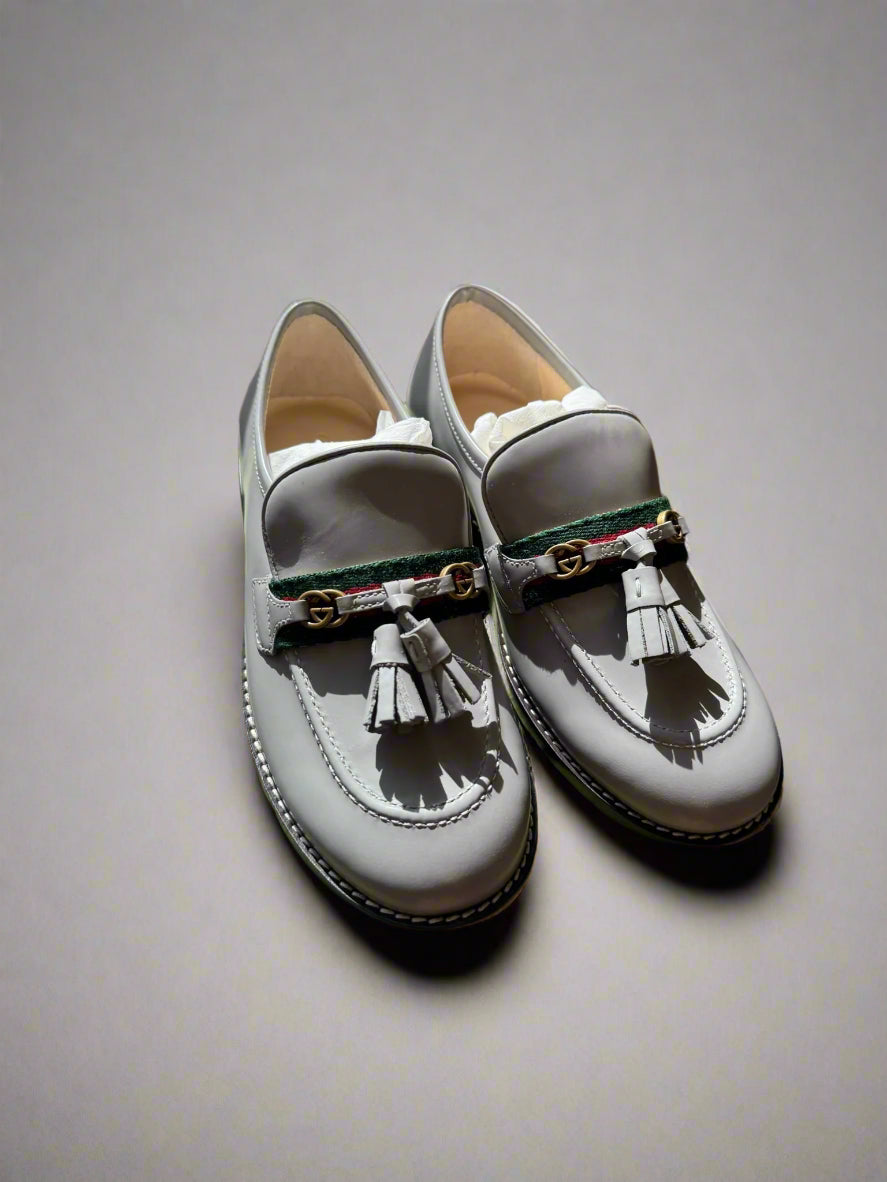 Pair of gray loafers with tassels on a green box